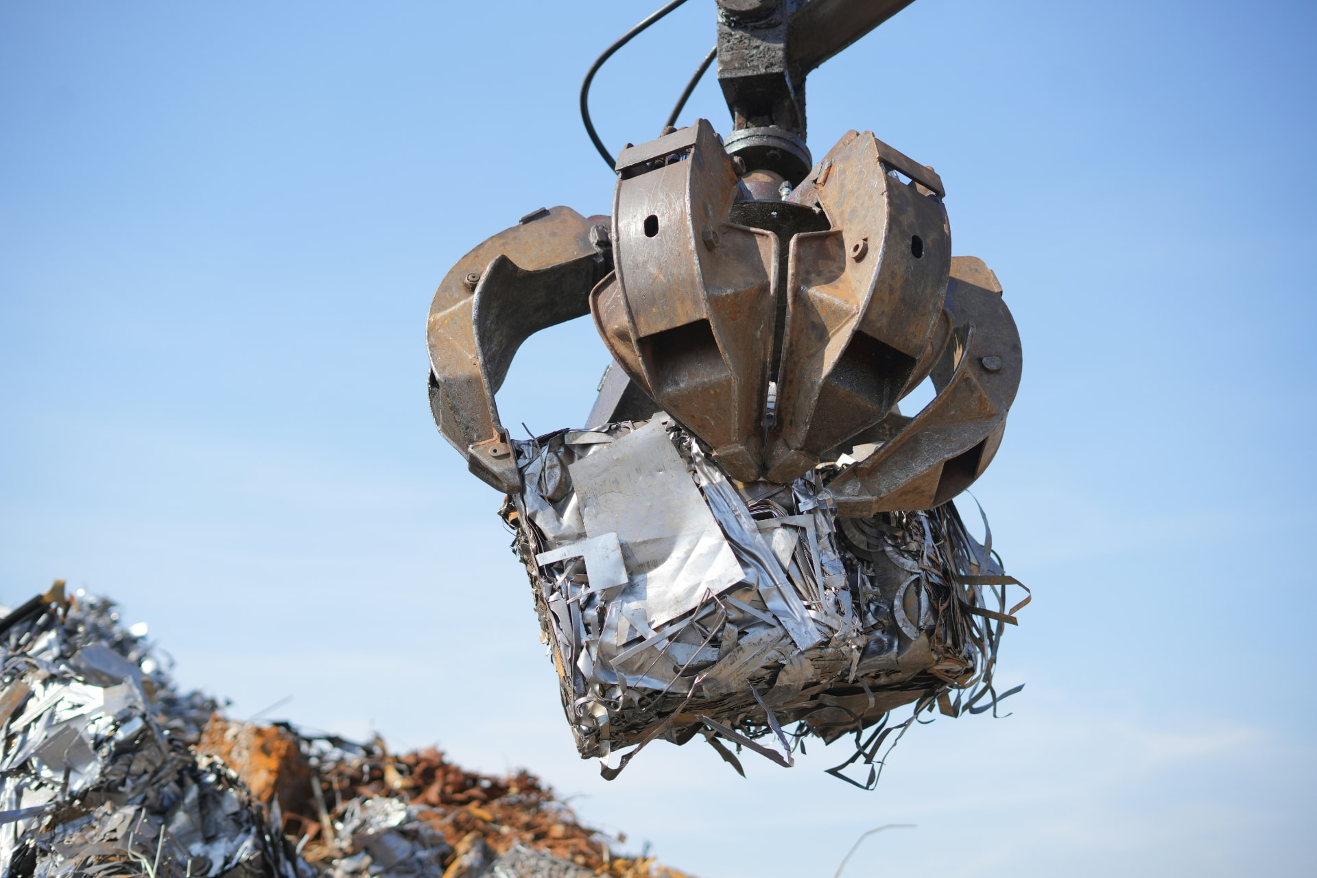 Kraangrijper tilt een samengeperst pakket autoschroot op een recyclagepark